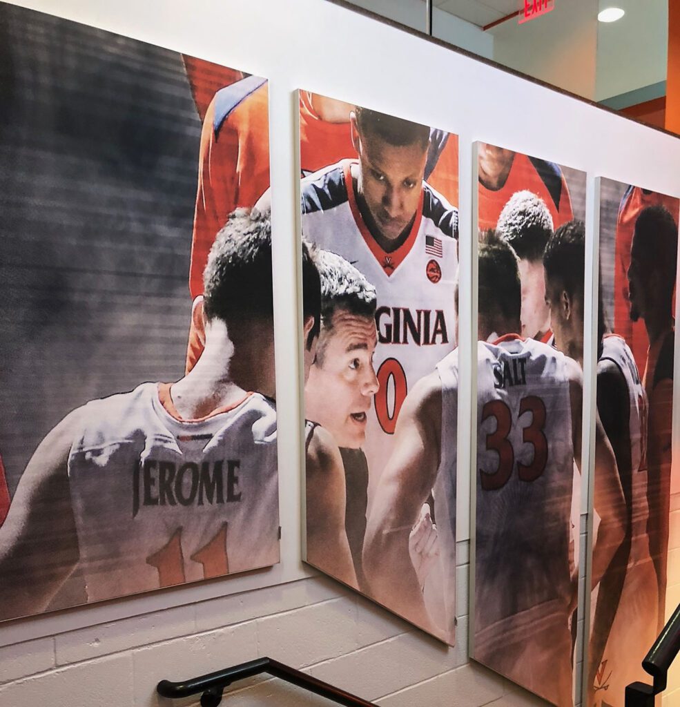 image features a large wall graphic or mural depicting members of the Virginia Cavaliers men's basketball team.